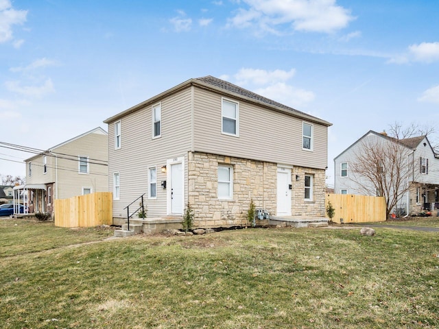 back of property with stone siding, fence, and a lawn