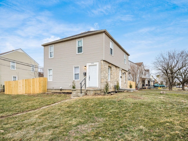 back of house with stone siding, fence, and a yard