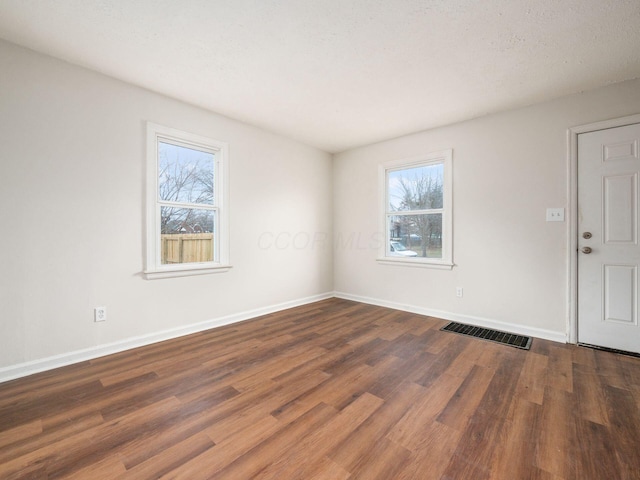 unfurnished room with baseboards, wood finished floors, visible vents, and a healthy amount of sunlight