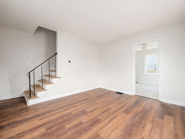 unfurnished room with stairway, wood finished floors, visible vents, and baseboards