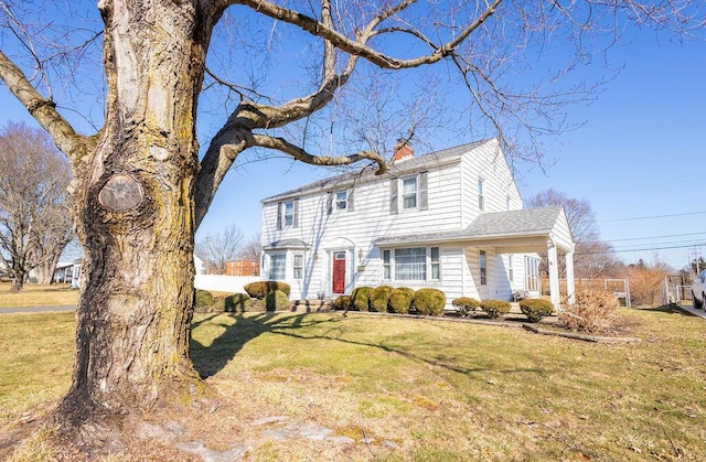 view of front of home featuring a front yard, roof with shingles, and a chimney