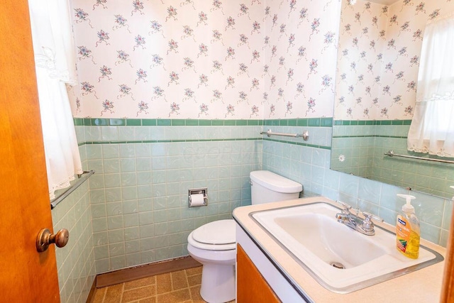 half bath featuring wainscoting, vanity, toilet, and wallpapered walls