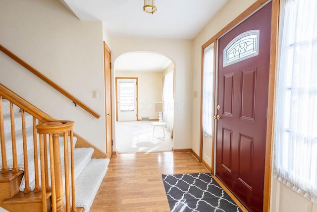 entryway featuring arched walkways, light wood finished floors, stairway, and baseboards