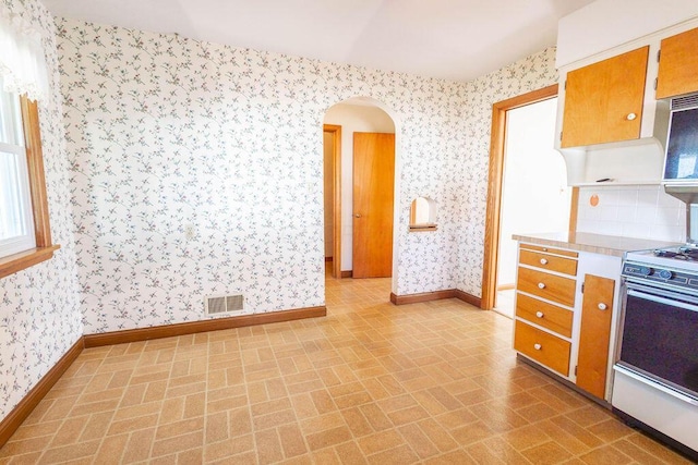 kitchen with wallpapered walls, gas range oven, visible vents, and arched walkways