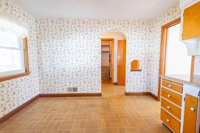 spare room with arched walkways, brick floor, visible vents, baseboards, and wallpapered walls