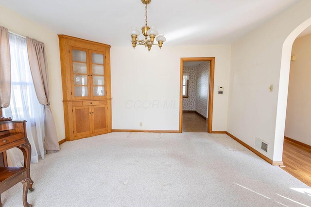 unfurnished room featuring arched walkways, light carpet, visible vents, and baseboards