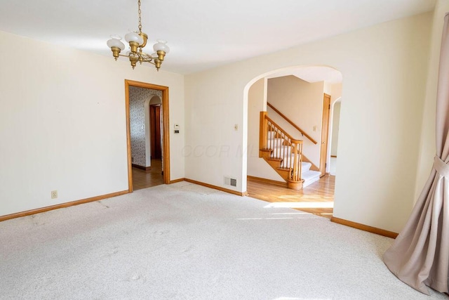 carpeted empty room featuring arched walkways, a chandelier, visible vents, baseboards, and stairs