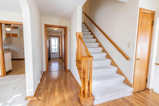 entryway with baseboards, arched walkways, stairs, and light wood-style floors