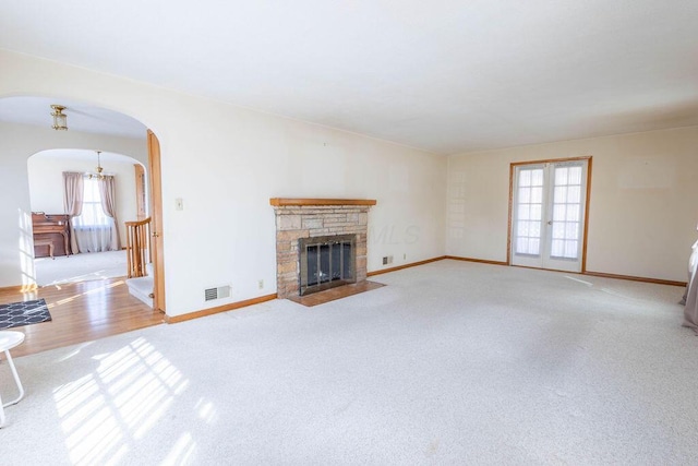 unfurnished living room with arched walkways, french doors, visible vents, a fireplace with flush hearth, and baseboards