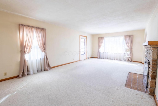 unfurnished living room with carpet flooring, a stone fireplace, and baseboards