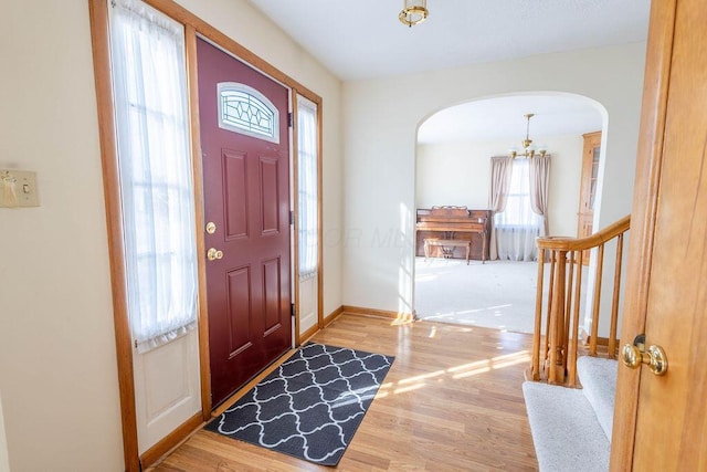 foyer entrance featuring baseboards, arched walkways, wood finished floors, stairs, and a chandelier