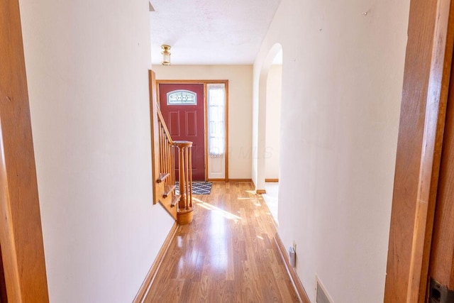 doorway to outside with arched walkways, light wood finished floors, visible vents, stairway, and baseboards