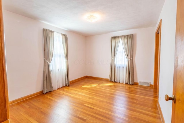 spare room featuring light wood-type flooring, visible vents, and baseboards