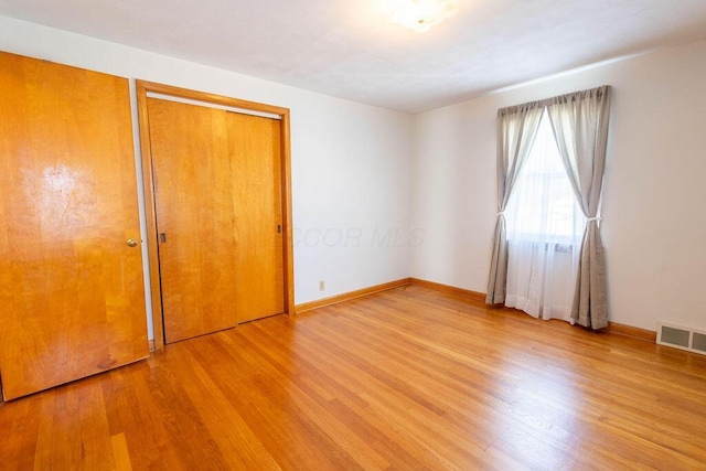 unfurnished bedroom featuring light wood-style flooring, a closet, visible vents, and baseboards