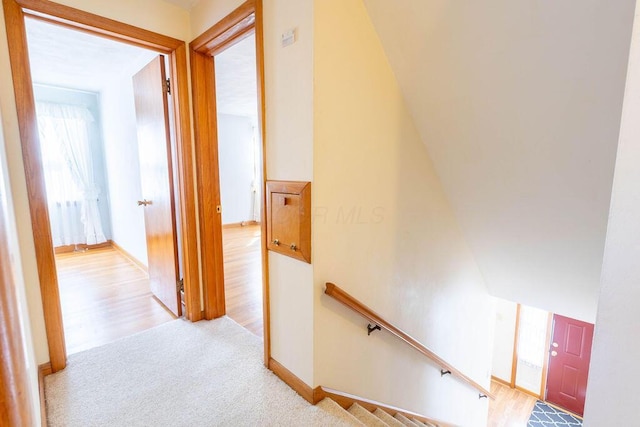 corridor featuring carpet floors, wood finished floors, an upstairs landing, and baseboards