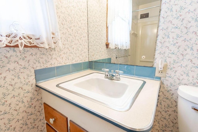 bathroom with visible vents, vanity, toilet, and wallpapered walls