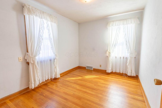 empty room featuring light wood-type flooring, visible vents, and baseboards