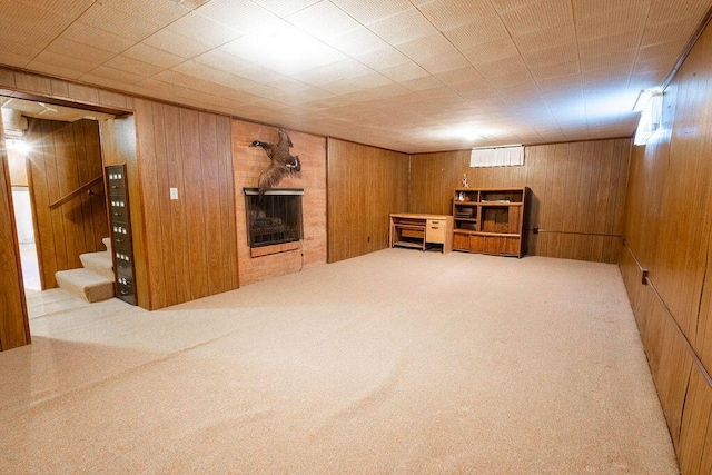 finished below grade area featuring stairs, wood walls, carpet, and a brick fireplace