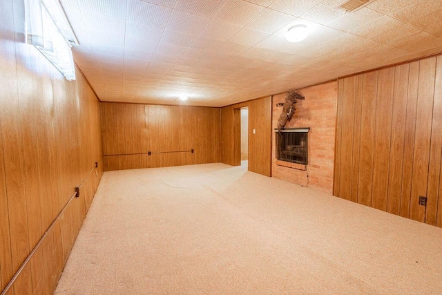 finished basement with wood walls, a brick fireplace, visible vents, and light colored carpet