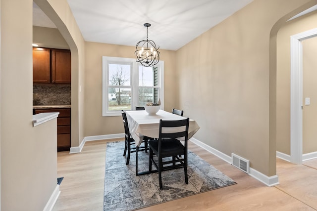 dining space featuring light wood finished floors, baseboards, visible vents, and arched walkways