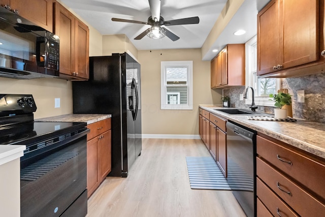 kitchen with light wood-style flooring, a sink, baseboards, decorative backsplash, and black appliances