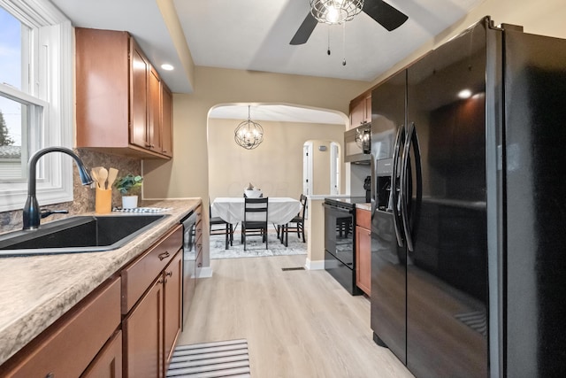 kitchen with arched walkways, decorative backsplash, brown cabinetry, a sink, and black appliances