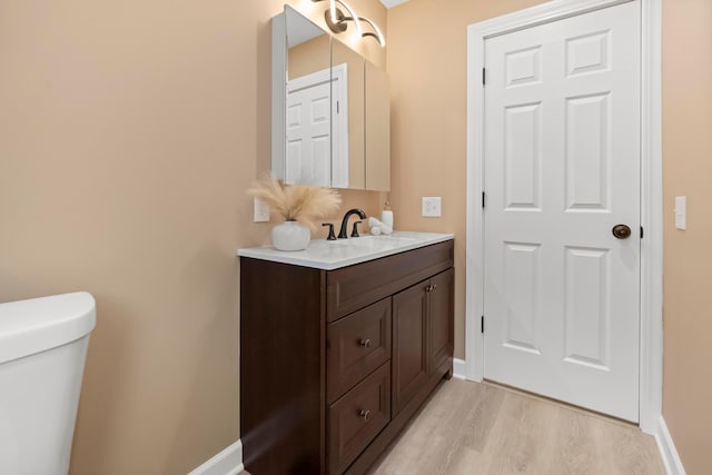 half bathroom featuring baseboards, wood finished floors, and vanity