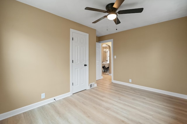 spare room with visible vents, ceiling fan with notable chandelier, light wood-style flooring, and baseboards