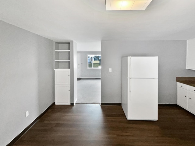 kitchen with dark wood-style flooring, white cabinetry, baseboards, freestanding refrigerator, and dark countertops