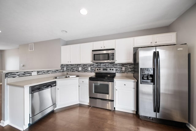 kitchen featuring stainless steel appliances, tasteful backsplash, white cabinets, a sink, and a peninsula