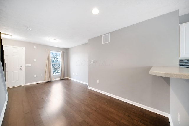 empty room with dark wood-style flooring, visible vents, and baseboards