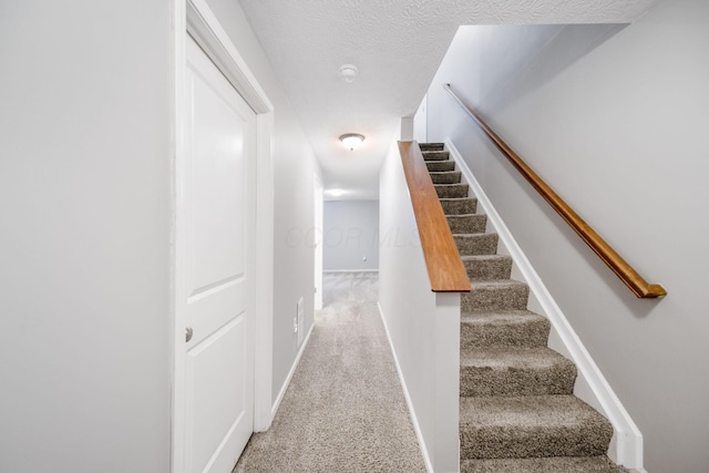 stairway featuring a textured ceiling, carpet floors, and baseboards