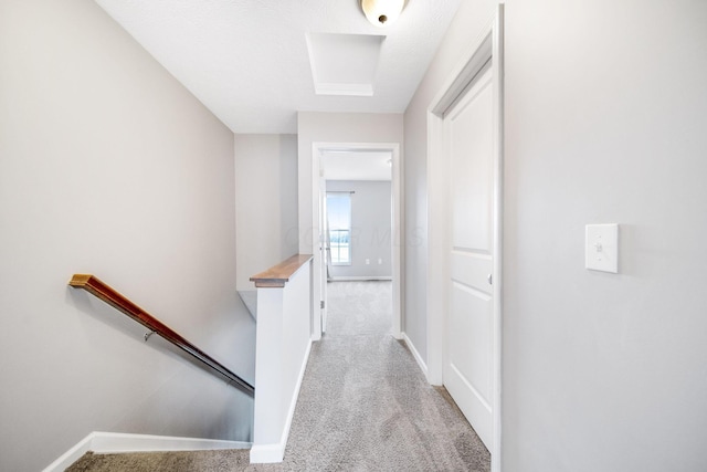 corridor featuring baseboards, an upstairs landing, and light colored carpet