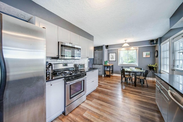 kitchen featuring light wood finished floors, stainless steel appliances, dark countertops, backsplash, and white cabinetry