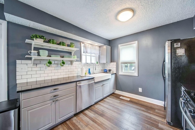 kitchen featuring light wood finished floors, baseboards, appliances with stainless steel finishes, a sink, and backsplash