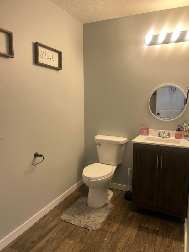 half bathroom featuring toilet, vanity, a textured ceiling, wood finished floors, and baseboards