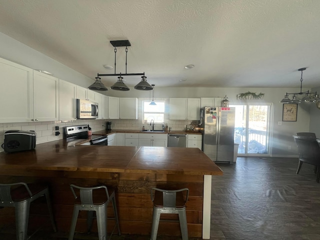 kitchen featuring tasteful backsplash, white cabinets, a peninsula, stainless steel appliances, and a sink