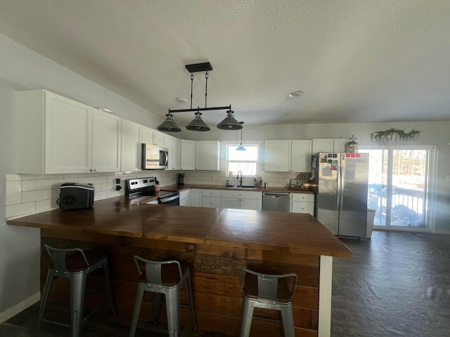 kitchen featuring a peninsula, a sink, white cabinetry, appliances with stainless steel finishes, and tasteful backsplash