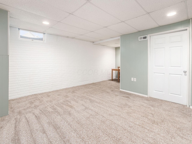 finished basement with brick wall, a drop ceiling, carpet flooring, and visible vents