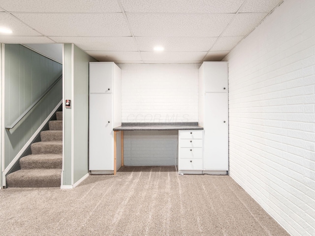 finished below grade area with a paneled ceiling, brick wall, and carpet flooring