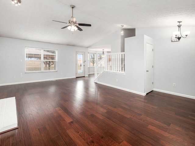 unfurnished living room with baseboards, dark wood-type flooring, stairs, vaulted ceiling, and ceiling fan with notable chandelier