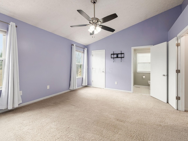 unfurnished bedroom with vaulted ceiling, a textured ceiling, carpet flooring, and connected bathroom