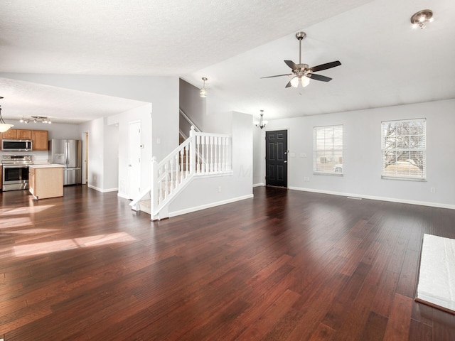 unfurnished living room featuring ceiling fan with notable chandelier, dark wood-style flooring, baseboards, vaulted ceiling, and stairway