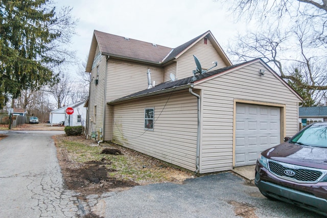 view of side of property with a garage, driveway, and a shingled roof