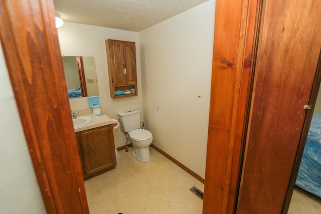 bathroom with a textured ceiling, toilet, vanity, baseboards, and tile patterned floors