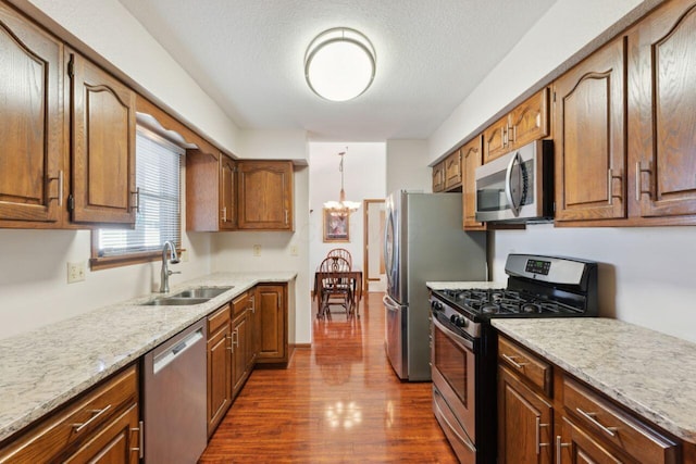 kitchen with appliances with stainless steel finishes, dark wood-type flooring, a sink, a textured ceiling, and a chandelier