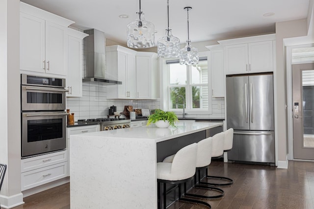 kitchen featuring appliances with stainless steel finishes, dark wood-type flooring, a kitchen island, and wall chimney exhaust hood