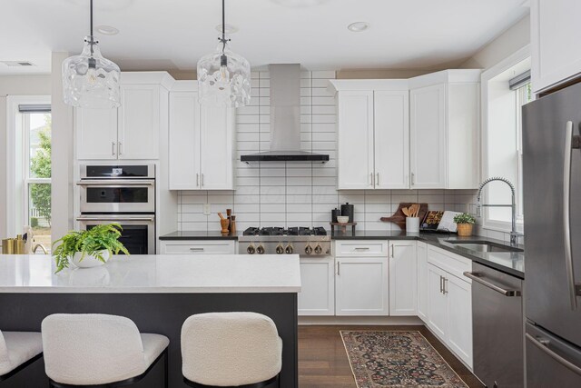 kitchen with a breakfast bar, backsplash, appliances with stainless steel finishes, a sink, and wall chimney exhaust hood