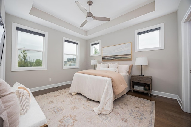 bedroom featuring a ceiling fan, a tray ceiling, baseboards, and wood finished floors