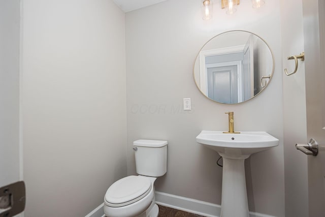 half bath featuring toilet, baseboards, and a sink